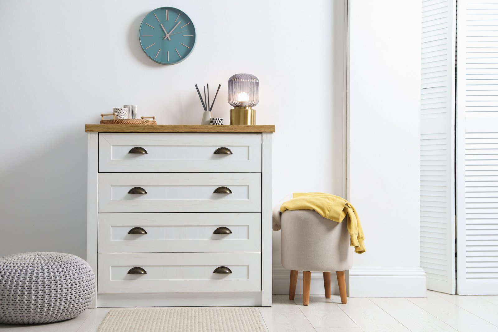Dresser with stylish reed diffuser and lamp near white wall indoors